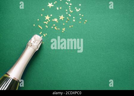 Christmas composition. Champagne bottle and golden confetti stars on green background. Festive flat lay, top view, copy space. Stock Photo