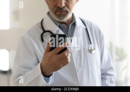 Close up focused mature doctor wearing uniform holding smartphone Stock Photo