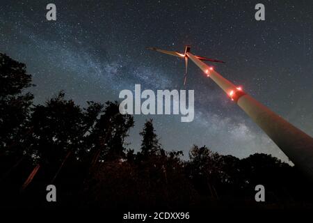 Industrial wind turbine amidst forest, nightshot with milky way and starry sky. Sustainabilty energy turnaround. Stock Photo