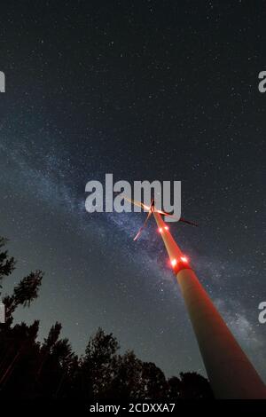 Industrial wind turbine amidst forest, nightshot with milky way and starry sky. Sustainabilty energy turnaround. Stock Photo