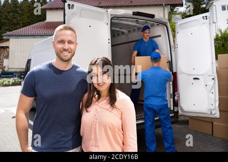 Happy Family Couple And Movers Unload Boxes From Truck Stock Photo