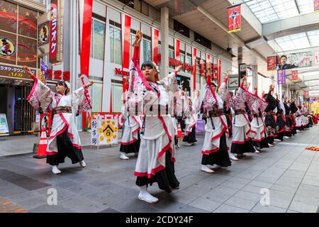 Japanese team of yosakoi dancers wearing long sleeved yukata and using naruko, wooden clappers, dancing in a shopping arcade, during Kyusyu Gassai.
