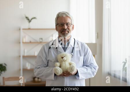 Head shot portrait mature pediatrician holding fluffy toy bear Stock Photo