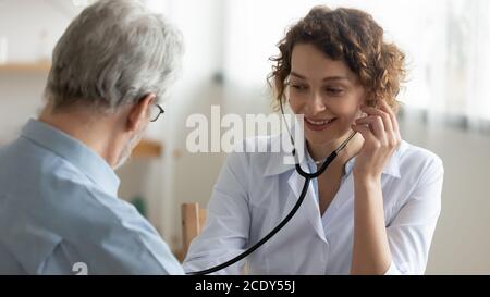 Smiling doctor using stethoscope, listening to mature patient heartbeat Stock Photo