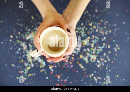 Crop female holding cup of hot coffee above confetti Stock Photo