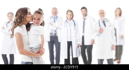 Mother kisses her daughter, team of doctors in medical clinic on background isolated on white Stock Photo