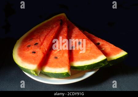 The Ripe watermelon in plate on black background.The Slices fruit with red pulp. Sweet products of the feeding Stock Photo