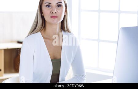 Business woman headshot while working with computer at the desk in modern office. Designer or female lawyer looks beautiful in white casual clothes Stock Photo