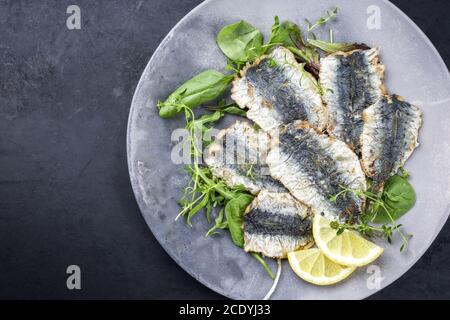 Fried sardines with lettuce and lemon slices offered as top view on a modern design plate with copy space left Stock Photo