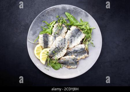 Fried sardines with lettuce and lemon slices offered as top view on a modern design plate with copy space Stock Photo