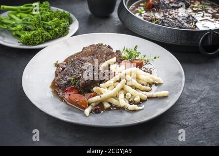 Traditional German braised beef cheeks in brown red wine sauce with noodles and broccoli offered as closeup on a modern design p Stock Photo