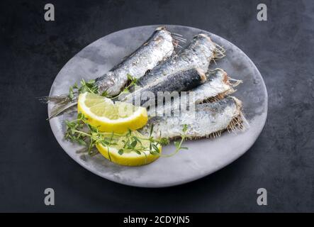 Fried sardines with lemon slices and herbs offered as closeup on a modern design plate with copy space Stock Photo