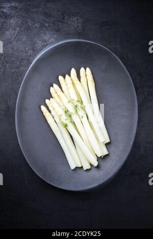 Traditional blanched white asparagus with herbs as top view on a cast iron modern design plate with copy space Stock Photo