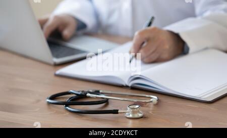 Close up mature doctor filling documents and using laptop Stock Photo
