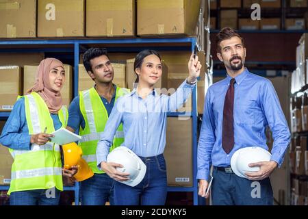 Group of Diversity warehouse worker checking and pointing to product when walking and meeting in local warehouse, muslim, indian, white caucasian and Stock Photo