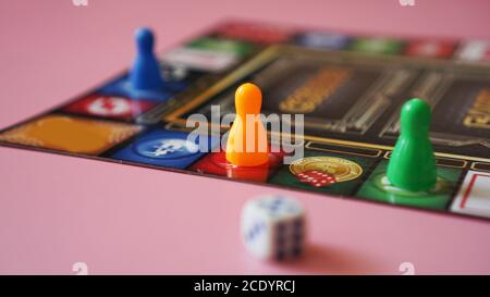 Colored board game figures with dice on pink background Stock Photo