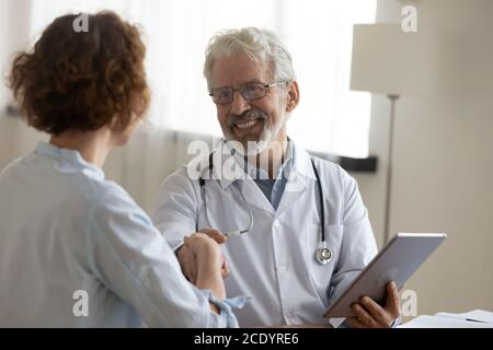 Smiling mature doctor shaking woman hand, holding digital tablet Stock Photo