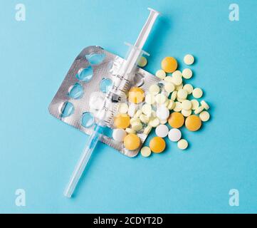 Medications and disposable syringe, different tablets in different colors on a blue background. Stock Photo