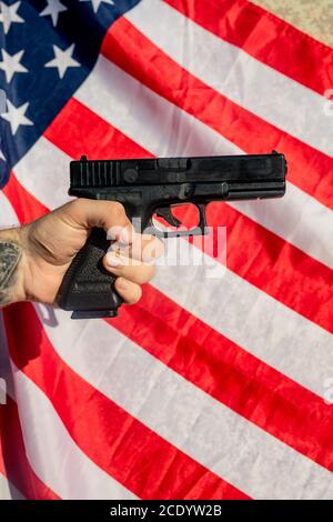 Tattooed hand holding gun against American flag, carrying of weapons concept Stock Photo