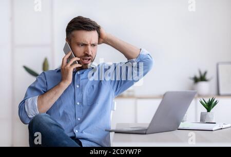Frustrated businessman having problems with computer, talking on cellphone with customer support Stock Photo