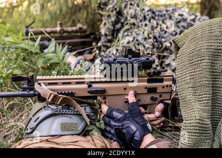 Snipers under camouflage nets lying in ambush and pointing rifles at enemy Stock Photo