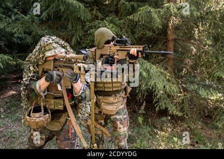 Focused army soldiers in camouflage shooting rifles while neutralizing enemy force Stock Photo