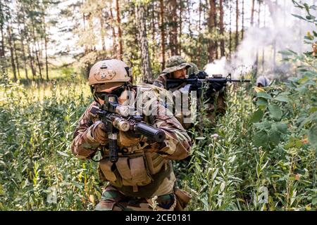 Group of soldiers in uniform moving through forest bushes while performing military reconnaissance operation Stock Photo