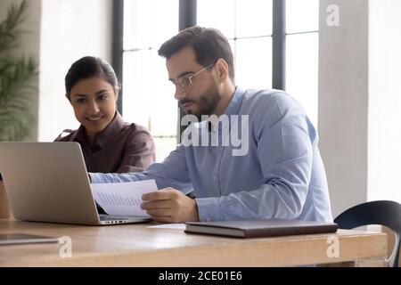 Focused young confident man working on computer with indian colleague. Stock Photo