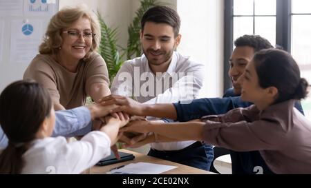 Positive happy young and old mixed race employees joining hands. Stock Photo
