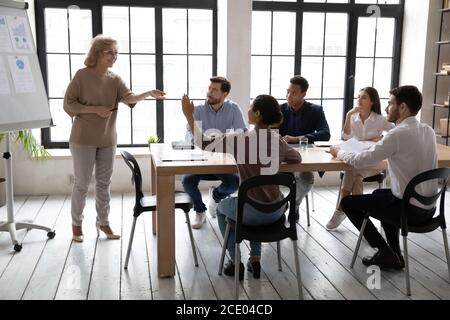 Young indian woman raising hand, asking questions to older speaker. Stock Photo