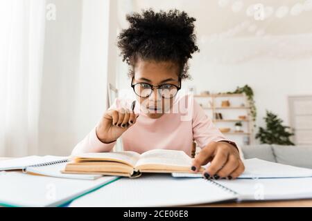 Shocked African Teen Girl Reading Book Doing Homework At Home Stock Photo