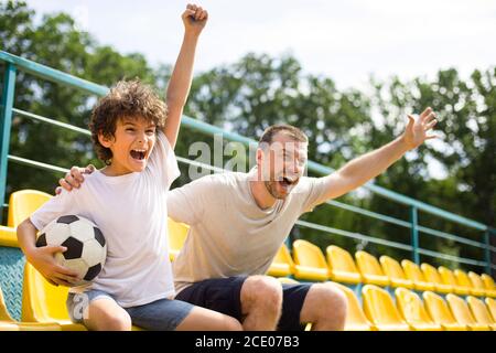 Dad and son watching football game on stadium and cheering Stock Photo