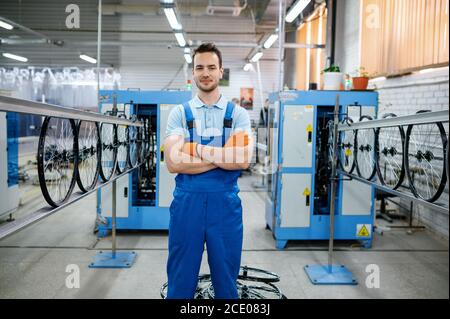 Worker in uniform poses on bicycle wheel factory Stock Photo