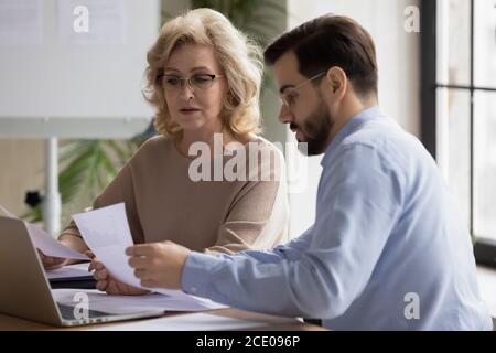 Focused middle aged 50s businesswoman discussing reports with employee. Stock Photo