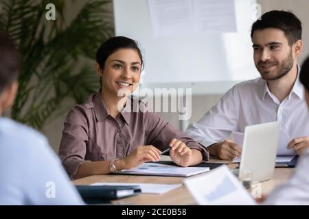 Smiling young indian female manager listening to colleagues. Stock Photo