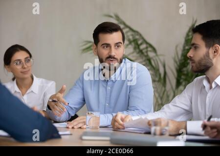 Motivated focused diverse teammates listening to male european colleague. Stock Photo