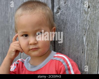Cute mixed race toddler boy (Caucasian and East Asian) poses for the camera with his hand to his cheek (thinking pose). Stock Photo
