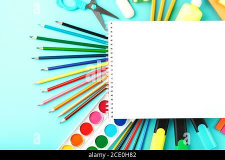 An album for creative development at school, with stationery on a cyanide background. A palette of colored paints, markers, brushes and pencils. Stock Photo