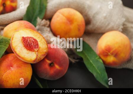 Peach fruit on a black background with a cloth of burlap and green leaves. Stock Photo