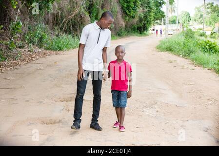 father walks with his young son in summer along the path in the park, the father holds the little son by the hand Stock Photo