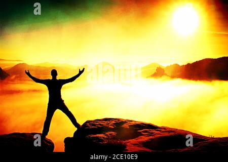 Film grain. Jumping hiker in black celebrate triumph between two rocky peaks. Wonderful daybreak. Stock Photo