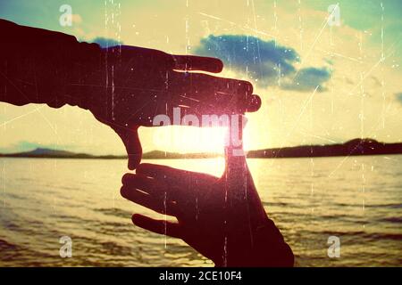 Film grain. Holding hands in square frame with sunset immersing at the horizon. Autumn evening at the lake. Stock Photo