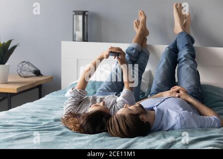 Relaxed young couple lying on bed, posing for selfie on smartphone. Stock Photo