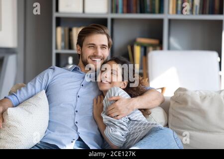 Happy young married couple embracing relaxing on sofa. Stock Photo