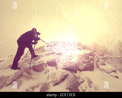 Abstract.  Travel photographer doing pictures in ancient stones on snowy peak Stock Photo