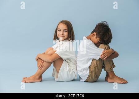Couple of children of roughly the same age sitting on the floor back to back Stock Photo