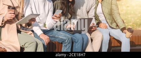 Cropped of international friends using diverse gadgets in park Stock Photo