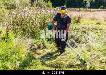Man striming an overgrown garden, using an industrial strimer and wearing a protection visor, Kilwinning, Ayrshire, Scotland, UK