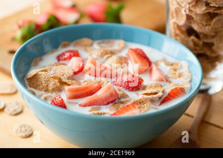 Whole grain flakes with milk and strawberries. Breakfast cereals with milk in blue bowl Stock Photo