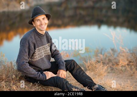 Young man traveler in black hat outdoor mountains lake on background. Autumn vacations and Lifestyle concept Stock Photo